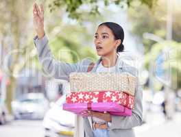 Woman holding gift and calling for a taxi in the street for travel to a birthday, anniversary or congratulation party. City girl standing in the road after shopping for a present for friend or family