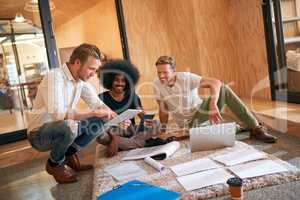 Combining their skills and know-how to reach success. a team of designers brainstorming on the floor in an office.