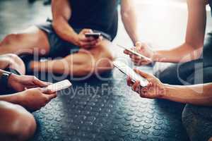 Downloading the latest fitness apps. Closeup shot of a group of people using their cellphones together at the gym.
