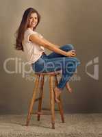 Shes a pretty girl with pretty vibes. Studio shot of a beautiful young woman sitting on a stool against a plain background.