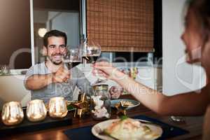 Cheers. an affectionate young couple toasting while enjoying a meal at home.