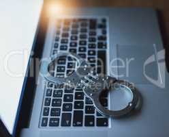 Protect your data before its too late. a pair of handcuffs lying on a laptop keyboard in the dark.
