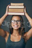 Anatomy of a bookworm. Studio shot of a young woman holding a pile of books against a grey background.