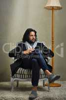 Hes a gentleman of leisure. a stylishly dressed man sitting on a chair in the studio.