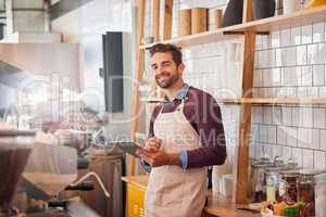 Coffee inspiration is never out of my reach. happy young business owner using a tablet while standing in his coffee shop.