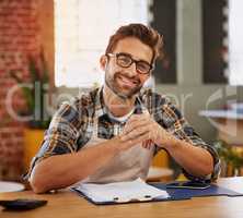 Admin keeps my business running. Portrait of a happy young business owner doing admin at a table in his coffee shop.