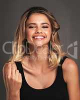 Shes got a charming smile and personality to match. Studio portrait of an attractive young woman twirling her hair against a dark background.