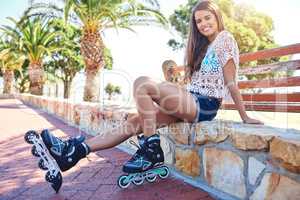 Like my wheels. Portrait of smiling young woman sitting on a bench in a park wearing rollerblades.