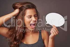 Speak your truth...or shout it. Studio shot of an attractive young woman holding a blank speech bubble and shouting against a gray background.