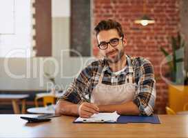 Admin is the pulse of every successful business. Portrait of a happy young business owner doing admin at a table in his coffee shop.