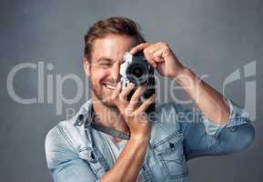 Seeing life through a lens. Portrait of a happy young man holding up a camera while posing against a gray background in the studio.