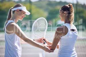 Tennis, trainer and professional female helping a friend with her racket on an outdoor sports court. Supportive, caring and happy woman or team player assisting her partner for skill in the sport.