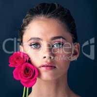 The rose isnt the only natural beautiful element here. Studio shot of an attractive young woman posing next to a couple of beautiful pink roses.