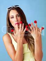 Who needs candy with these sweet babies. Studio shot of a woman eating raspberries off her fingertips against a blue background.