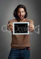 Take it from me. This is brilliant. Studio shot of an enthusiastic young man holding a digital tablet with a blank screen against a gray background.