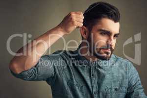 Wear that beard proudly. Studio shot of a handsome young man combing his hair against a grey background.