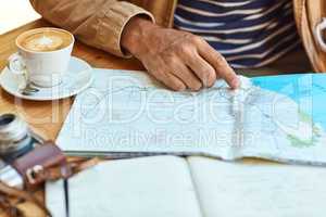 Getting to know his way around a new town. an unidentifiable tourist looking at maps and travel journals while enjoying coffee at a cafe.