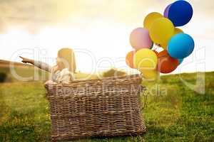 Im going over the rainbow. cute little girl playing outside with a basket and a bunch of balloons.