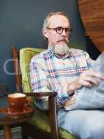 Coffee and newspaper, how I love to start my afternoons. a senior man reading the newspaper and having coffee at a coffee shop.