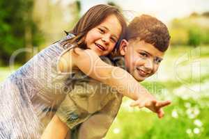 Sharing love and laughter. Portrait of an adorable little boy giving his little sister a piggyback ride outside.
