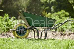 Farm or garden wheelbarrow on nature, agriculture environment or green countryside field used for farming work. Gardening equipment for lawn with sustainable grass, flower and plant growth