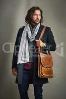 Never underestimate the power of a good outfit. a stylishly dressed man posing with a leather satchel in the studio.