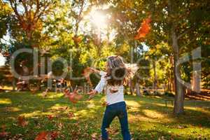 Nothing says fun like playing amongst the autumn leaves. a happy little girl playing in the autumn leaves outdoors.