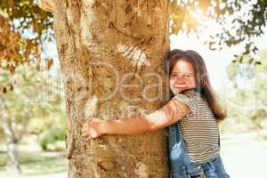 Nature is the best playground. Portrait of a little girl with her arms around a tree at the park.