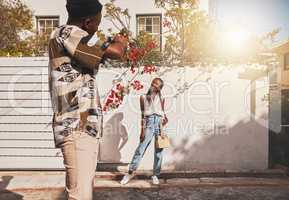 Photographer with model for summer fashion photography taking photo, posing and smiling for portrait shot with lens flare. African creative freelancer taking picture of young influencer woman outside